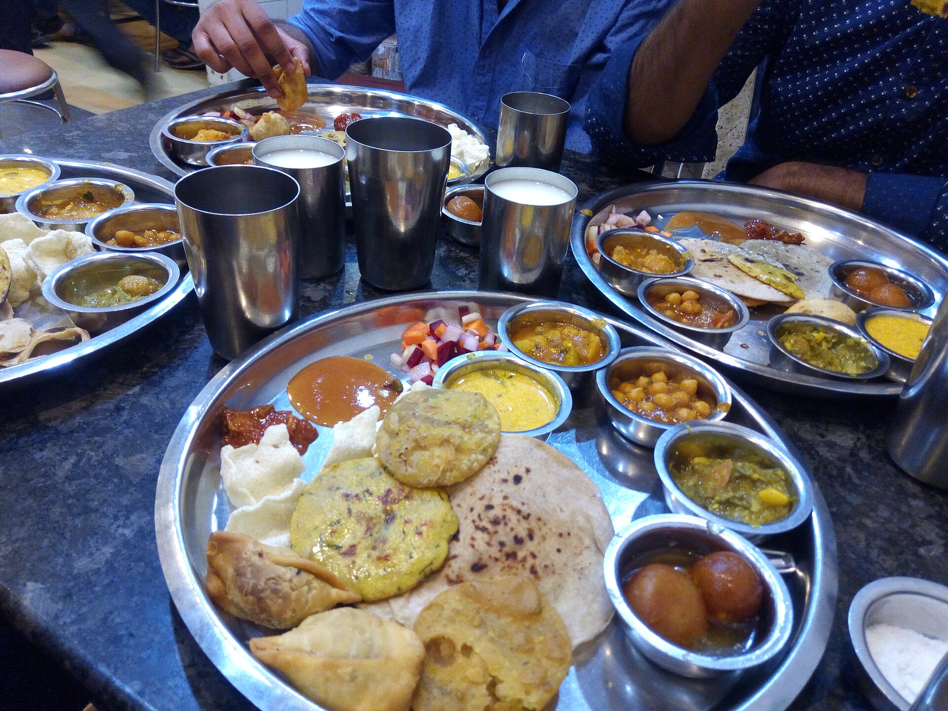 Several thalis laid out on one table for a group meal, with steel glasses of chaas